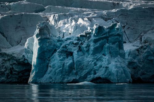 Free A striking image of a glacier's icy formations reflecting in calm waters, showcasing nature's raw power. Stock Photo