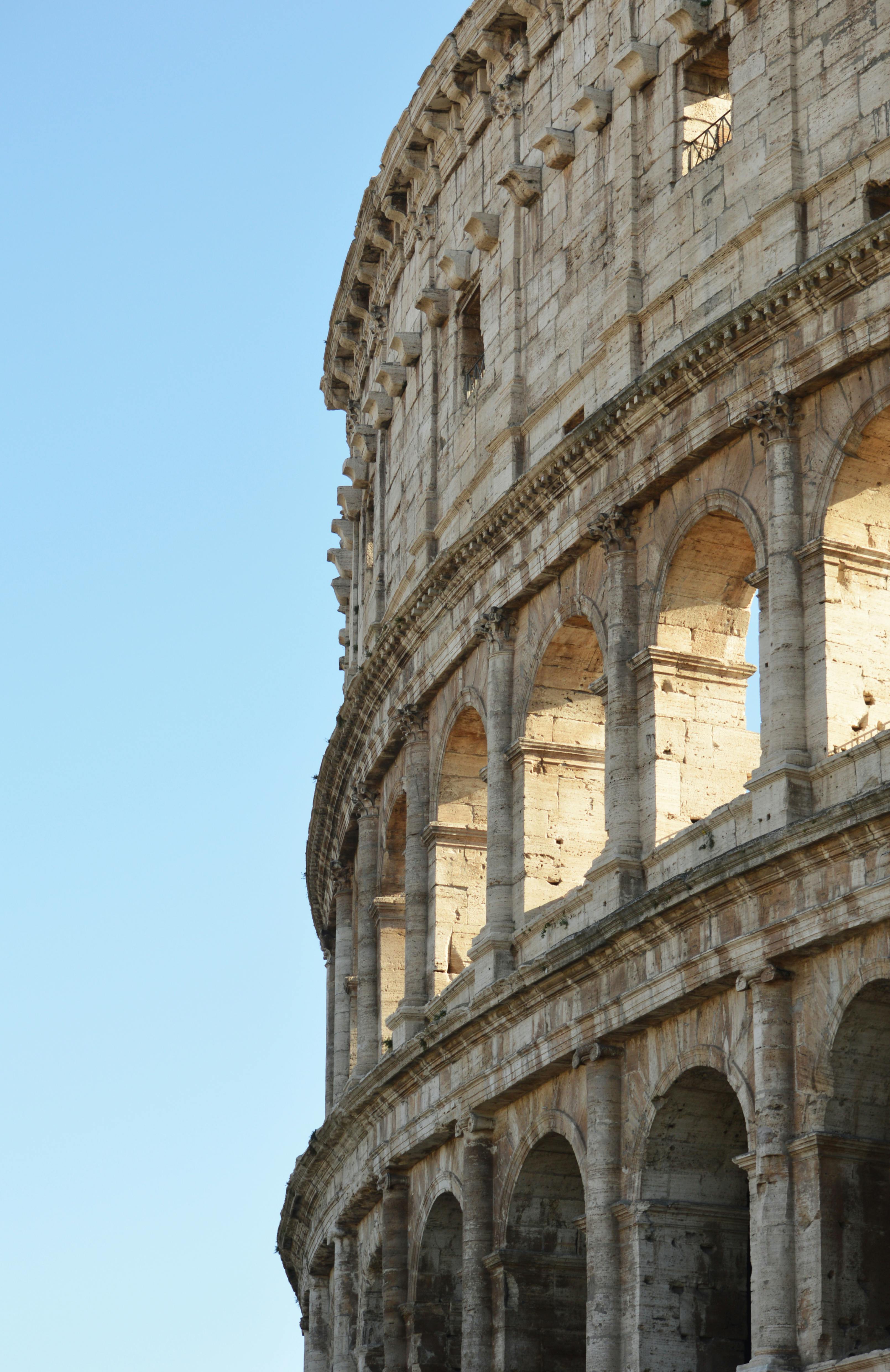 grátis Close do Coliseu em Roma com um céu azul claro, exibindo a arquitetura romana antiga. Foto profissional
