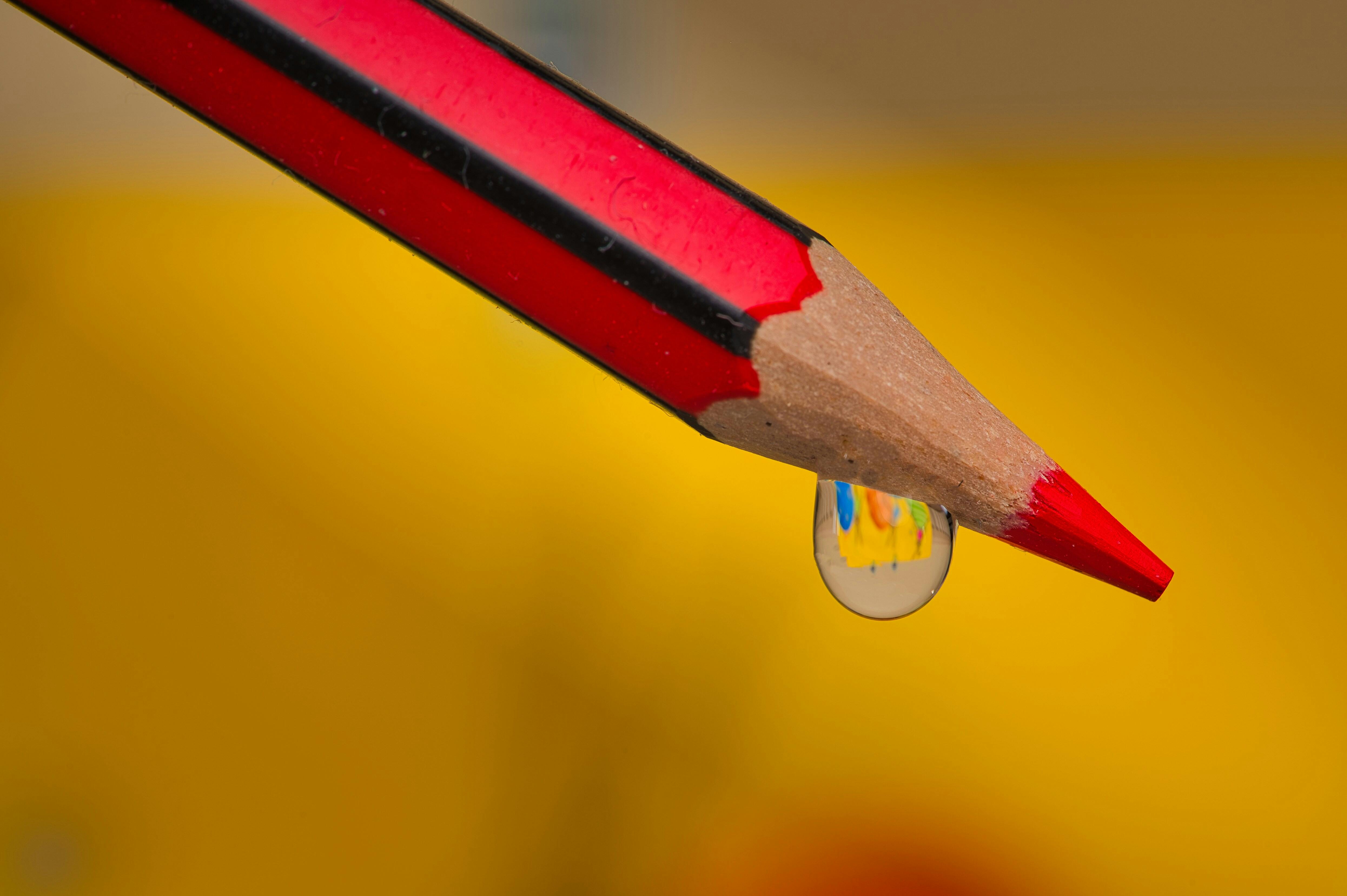 grátis Lápis vermelho com uma gota de água refletindo cores vibrantes, capturada em detalhes. Foto profissional