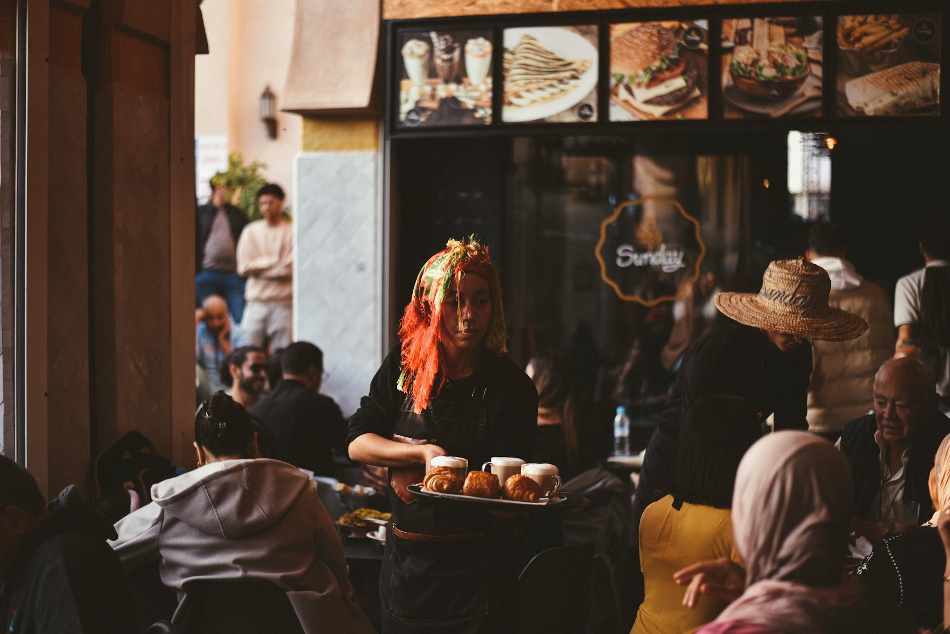 A bustling cafe in Agadir with a lively atmosphere and a waitress serving pastries.