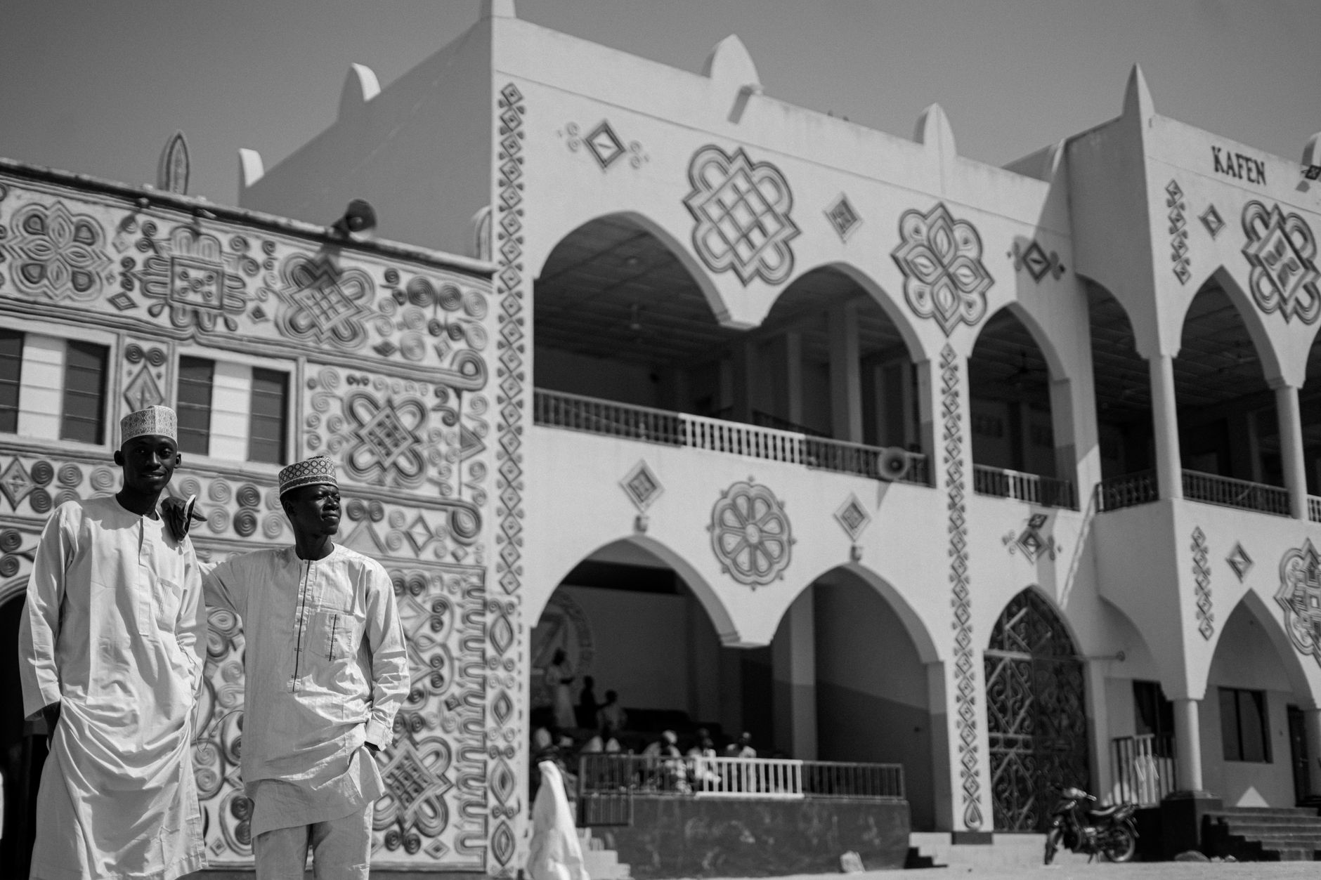 Two men stand in front of a vibrant traditional Nigerian building.