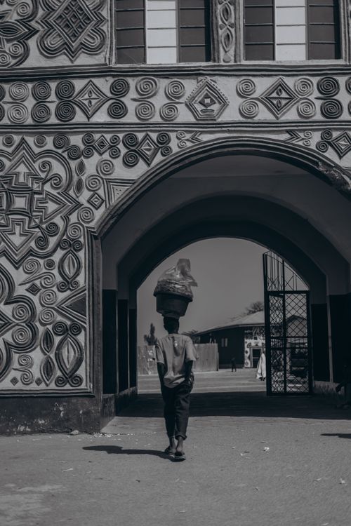 Free A person carrying goods on their head walks through ornate African architecture, illustrating cultural lifestyle. Stock Photo