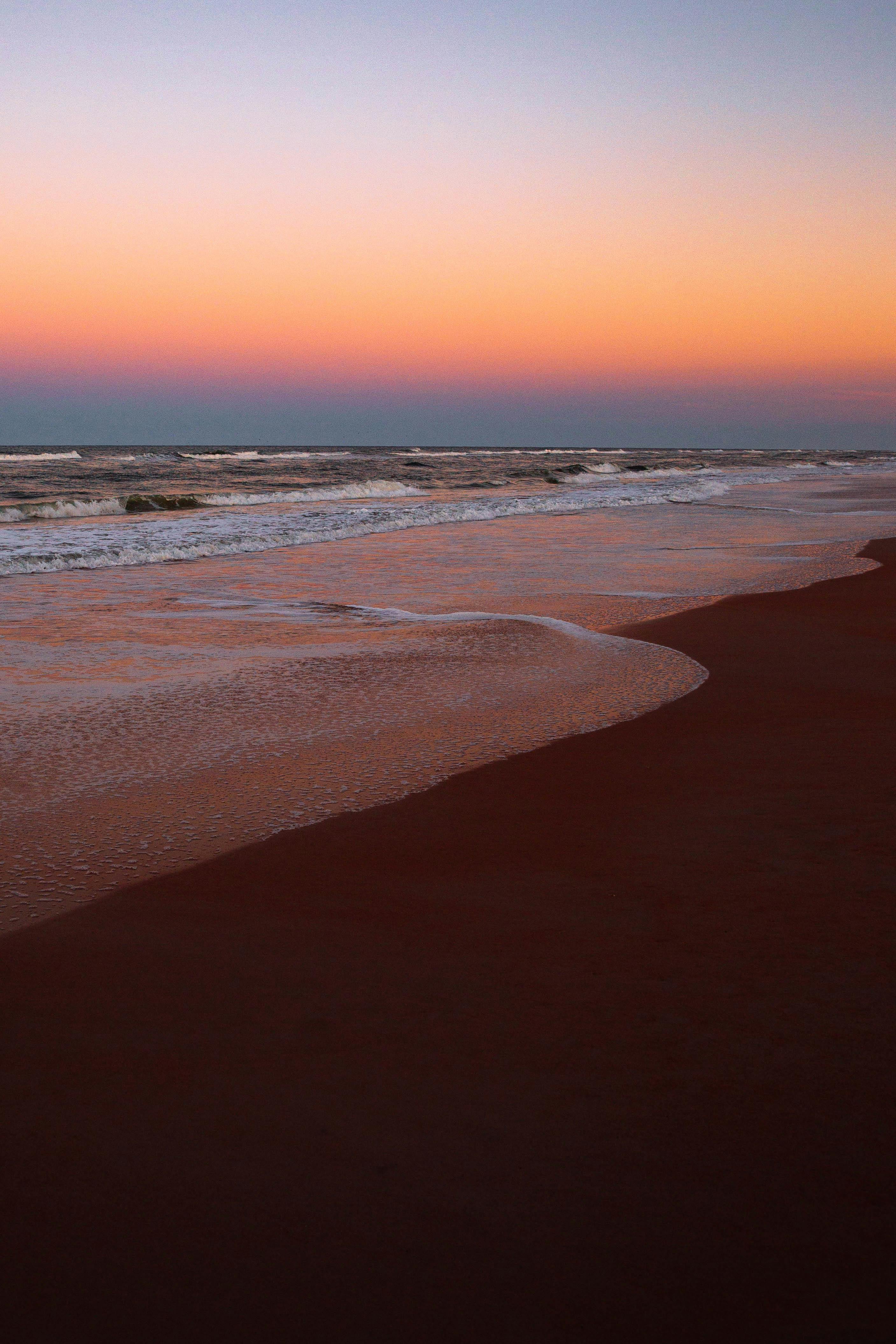 Peaceful beach scene at Ormond Beach during a stunning sunset, showcasing gentle waves and vibrant sky.