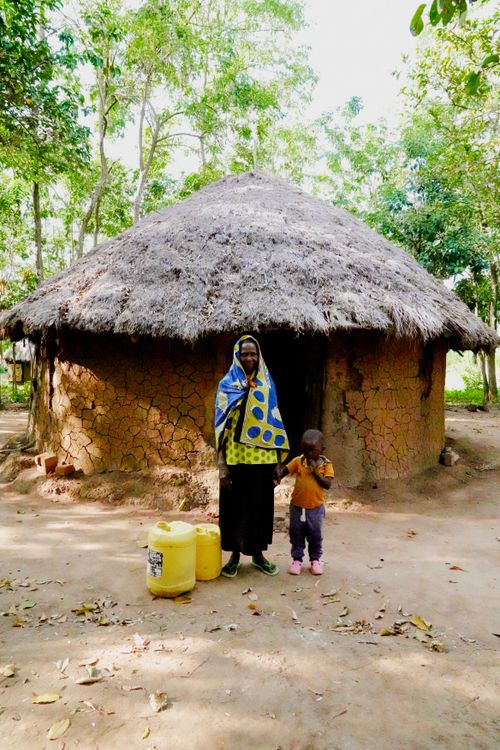 Free Mother and child standing outside a mud hut in a rural African village setting. Stock Photo