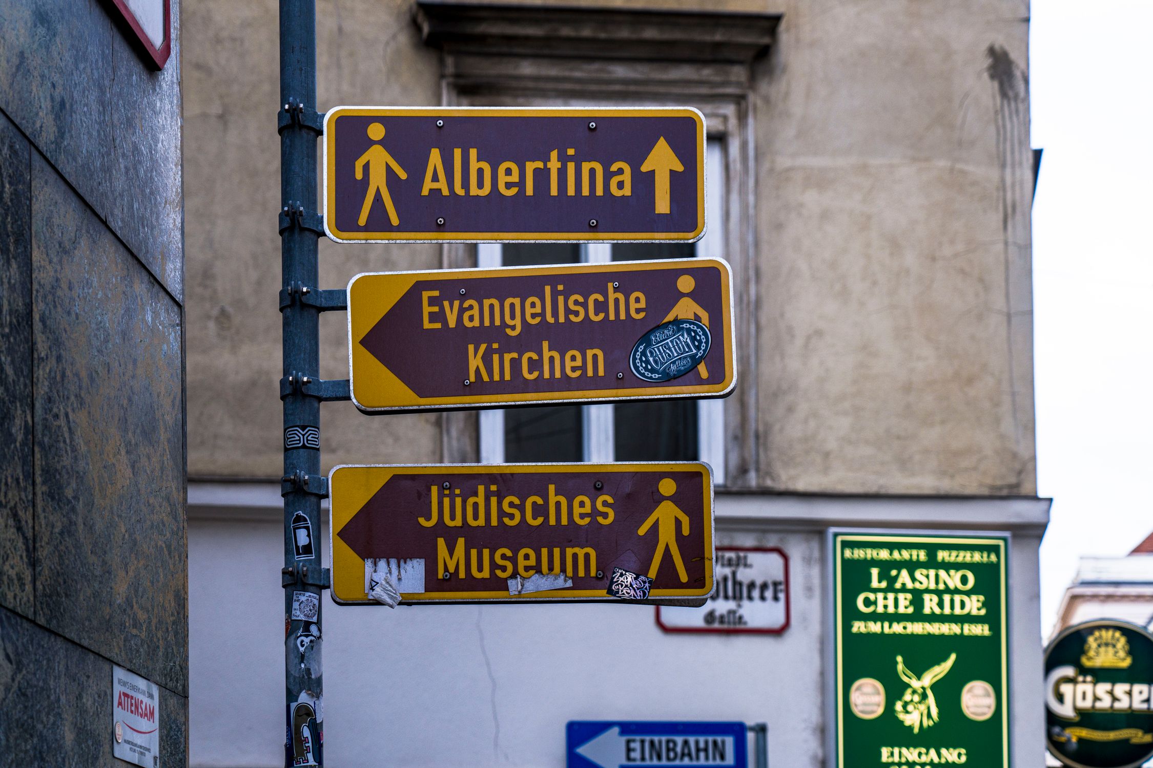 Street signs in Vienna guide tourists to Albertina, Evangelische Kirchen, and Jüdisches Museum.