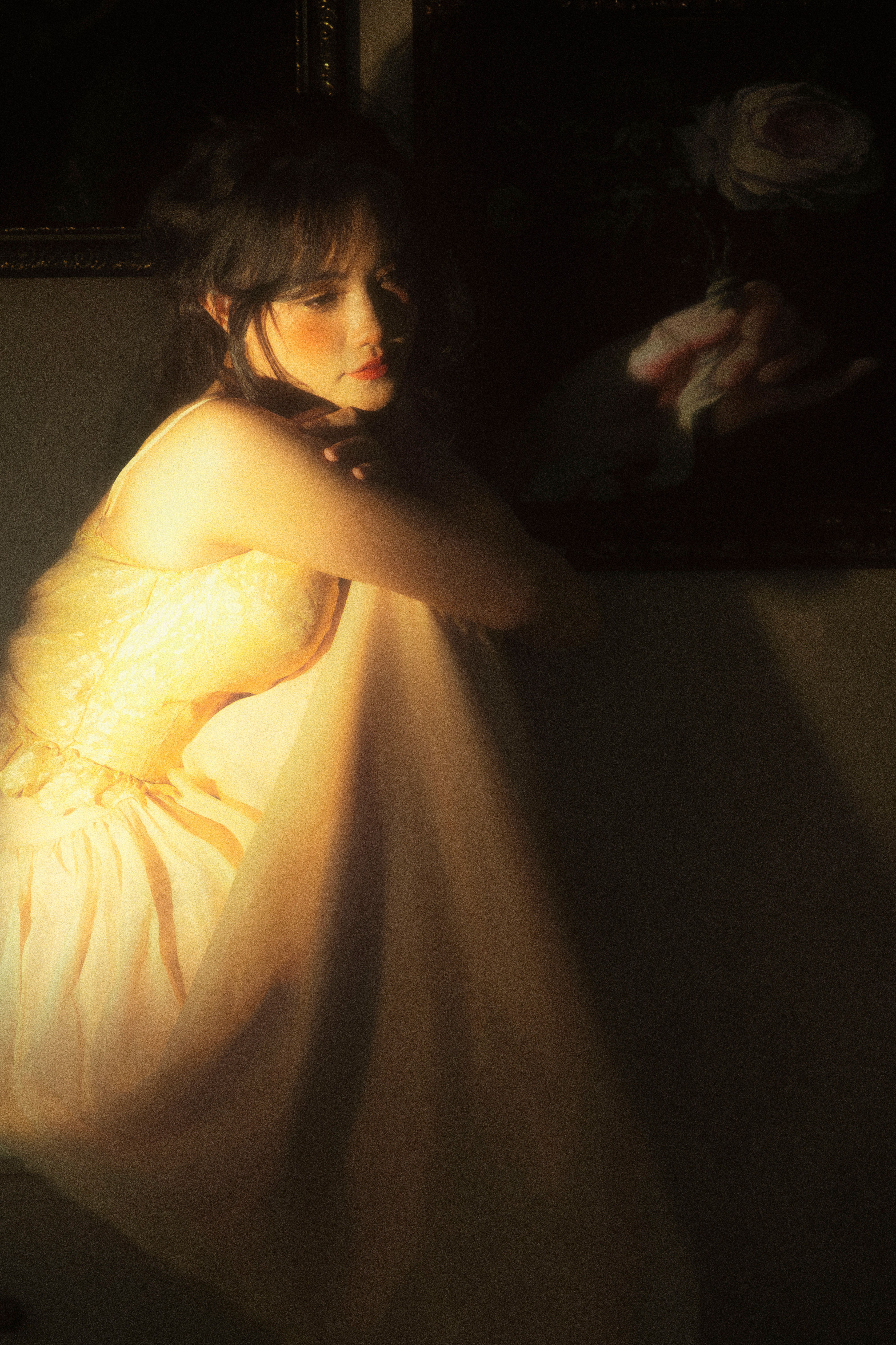 A contemplative woman in a light dress, captured in soft, warm lighting.