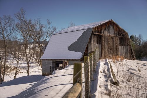 Free Charming rustic barn surrounded by a snowy winter landscape under a clear blue sky. Stock Photo