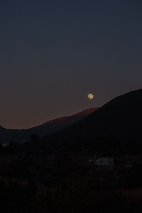 Free A serene full moon rises over a dark mountainous landscape at night. Stock Photo
