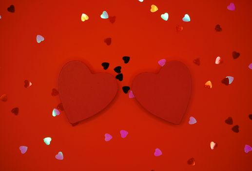 Two red hearts surrounded by colorful heart confetti on a red background, symbolizing love.