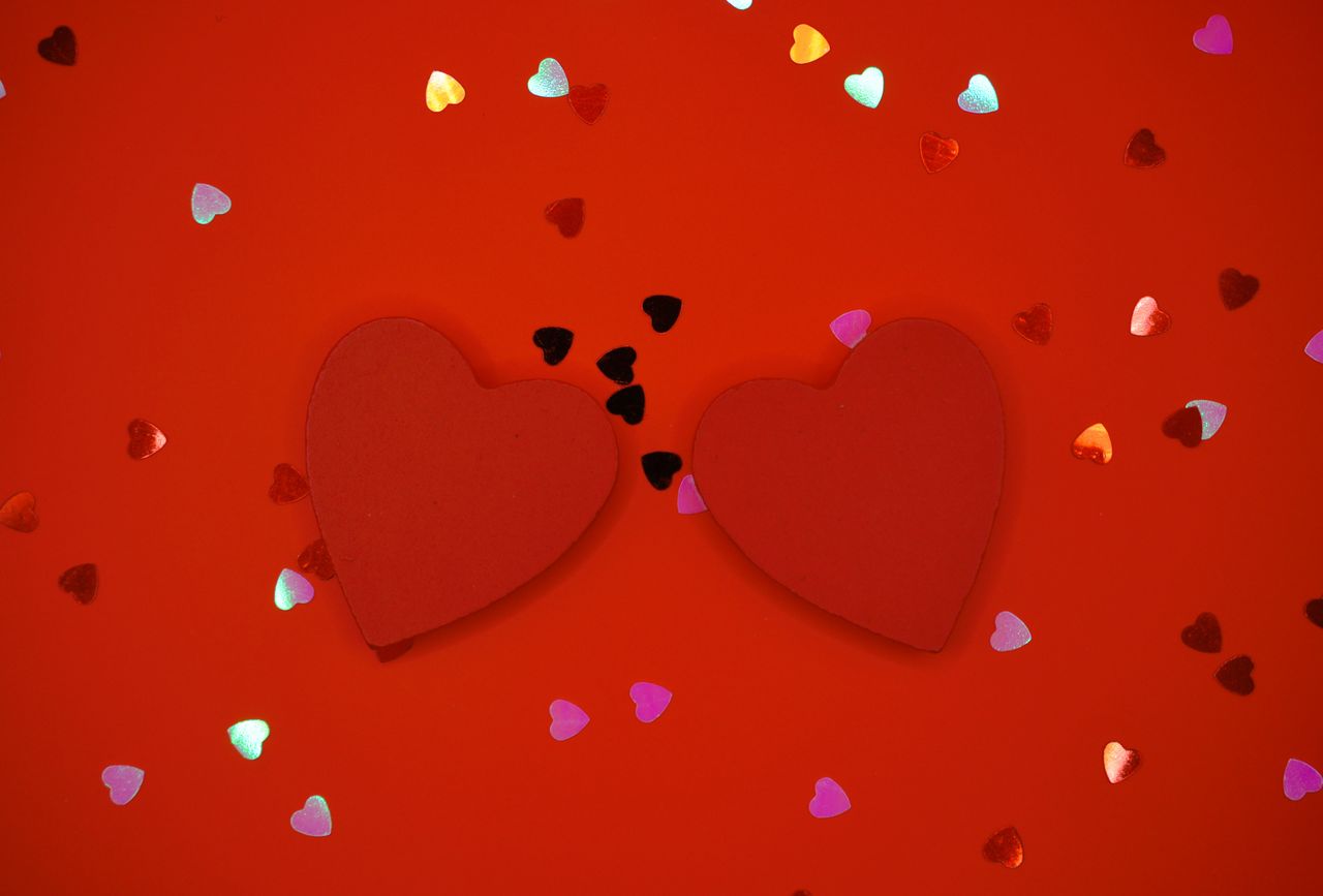 two red hearts surrounded by colorful heart confetti on a red backgrou