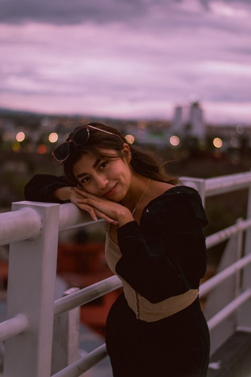 Free Smiling woman leaning on railing during evening on rooftop. Stock Photo