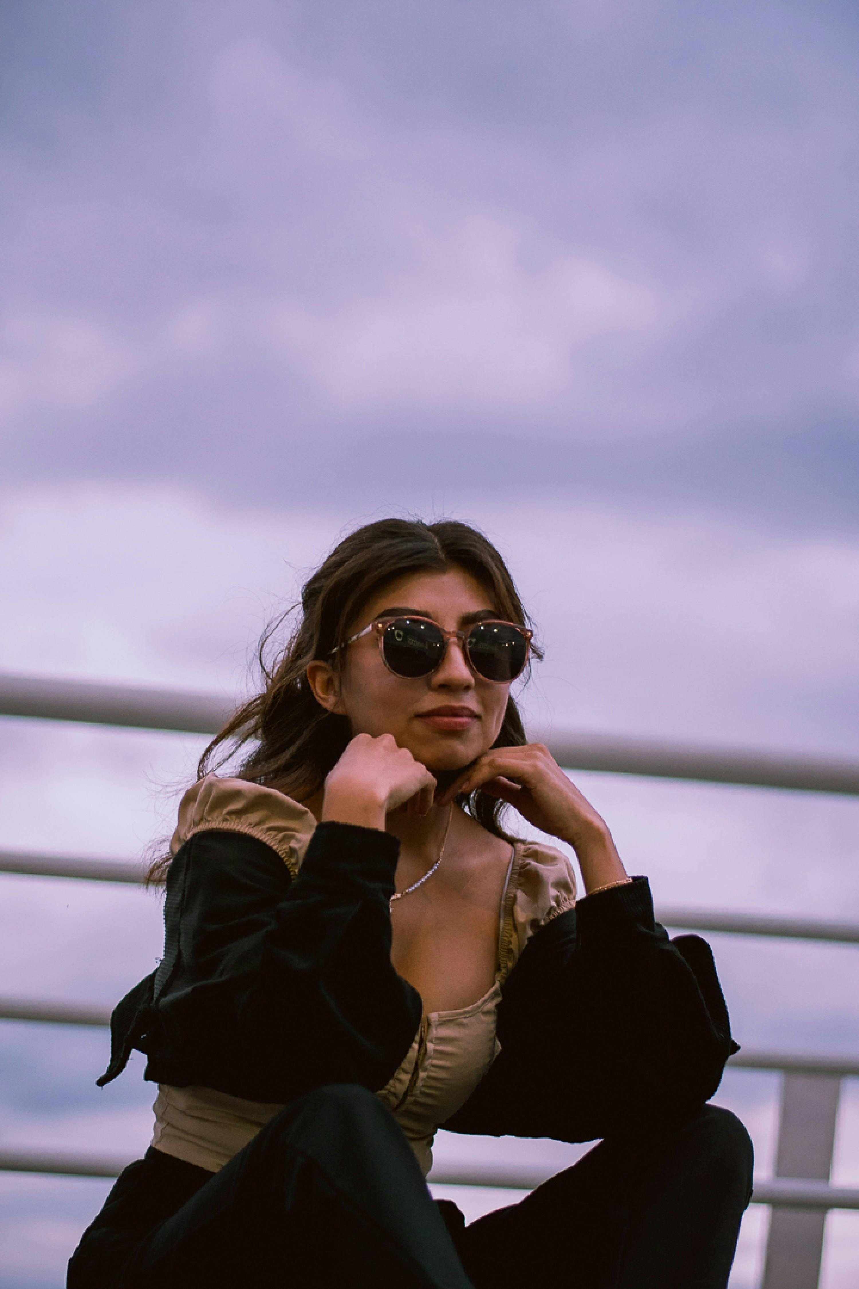 무료 야외에서 선글라스를 쓰고 생각에 잠긴 듯한 포즈를 취하고 있는 세련된 여성의 초상화입니다. 스톡 사진