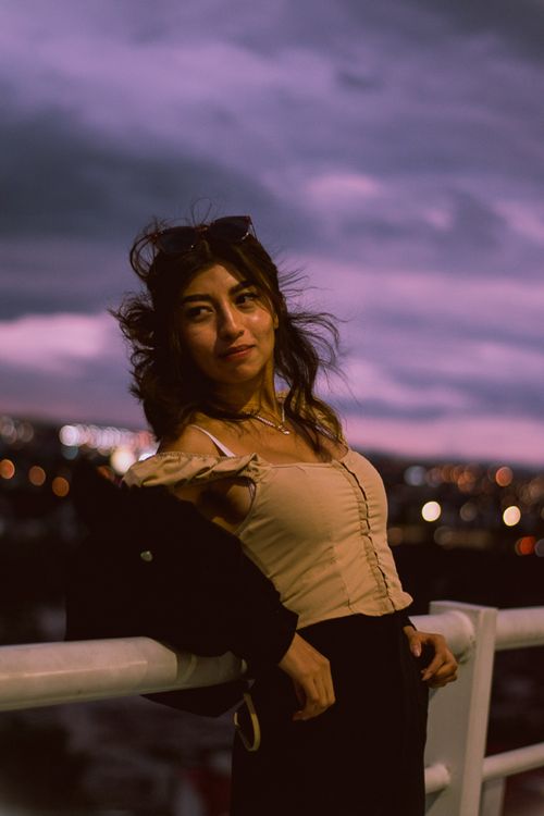 Free A woman stands gracefully on a rooftop at twilight with city lights in the background. Stock Photo