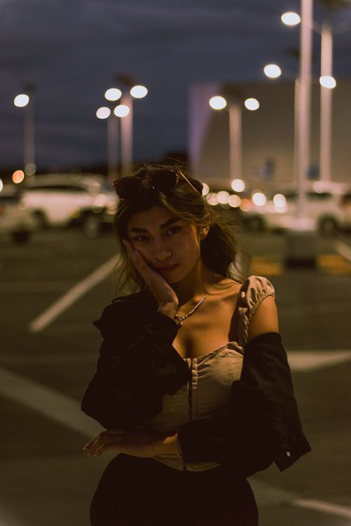 Free Young woman posing with city lights backdrop, exuding style and mystery. Stock Photo
