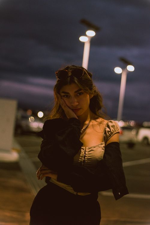 Free Stylish young woman poses at night under streetlights in urban setting, exuding a moody vibe. Stock Photo