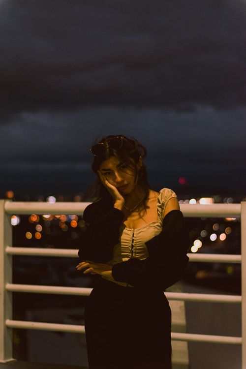 Free A woman stands thoughtfully on a terrace with city lights in the background. Stock Photo