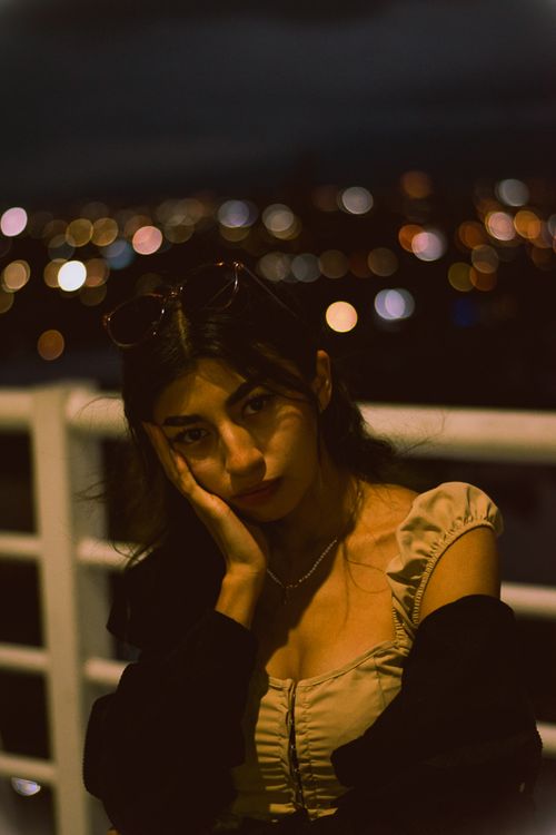 Free Portrait of a woman at night, highlighting moody ambiance and city light bokeh. Stock Photo