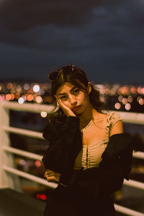 Free Thoughtful woman posing with city lights in the background at night, conveying a serene mood. Stock Photo
