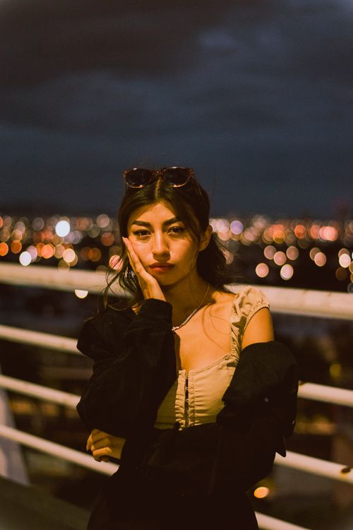 Free Stylish young woman posing pensively on a rooftop at night with city lights. Stock Photo