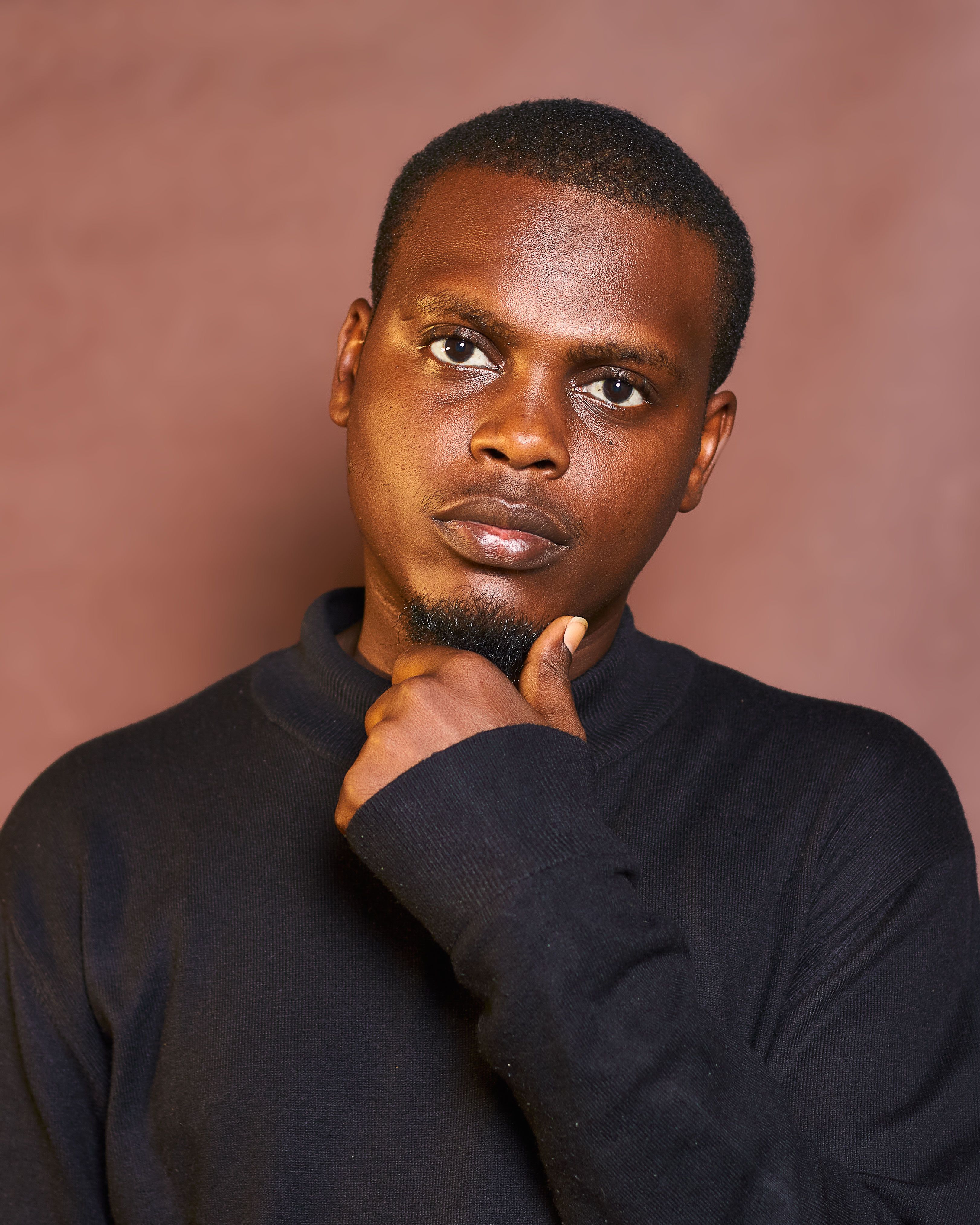 A pensive man poses against a neutral brown backdrop, exuding contemplation.