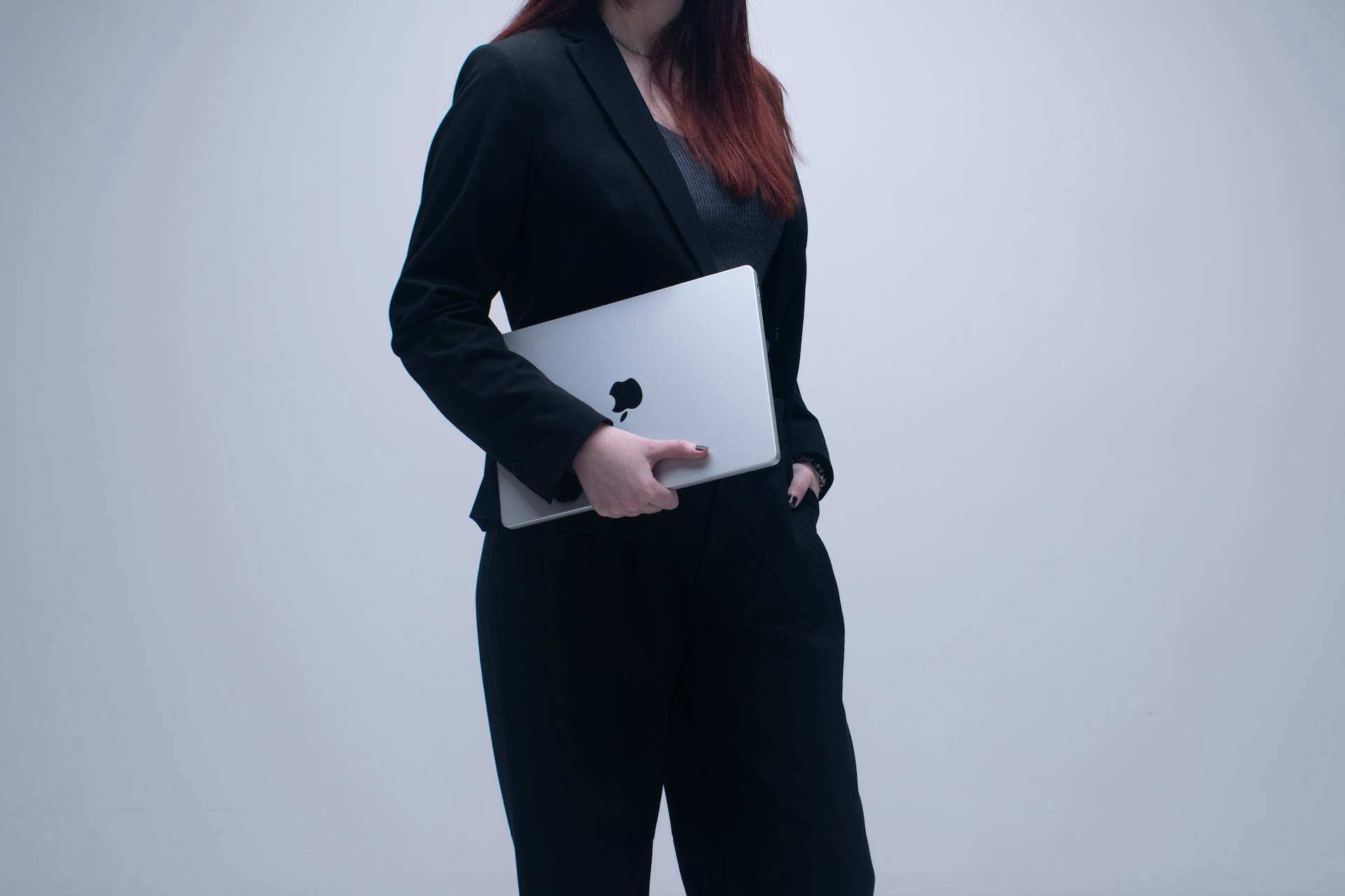 Businesswoman in a dark suit holding a laptop against a neutral background, symbolizing modern work culture.