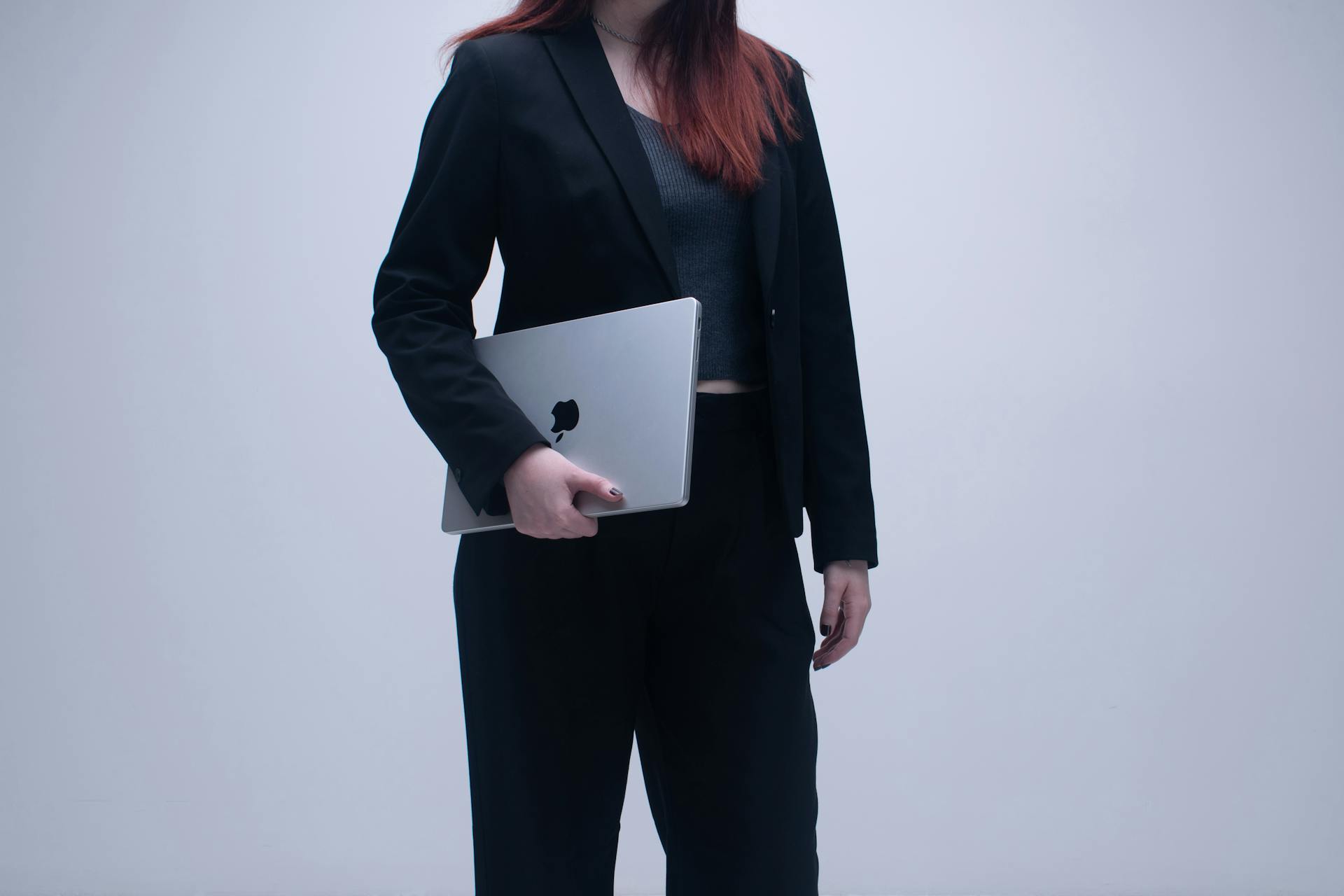 Businesswoman in black suit holding a laptop in an office setting.