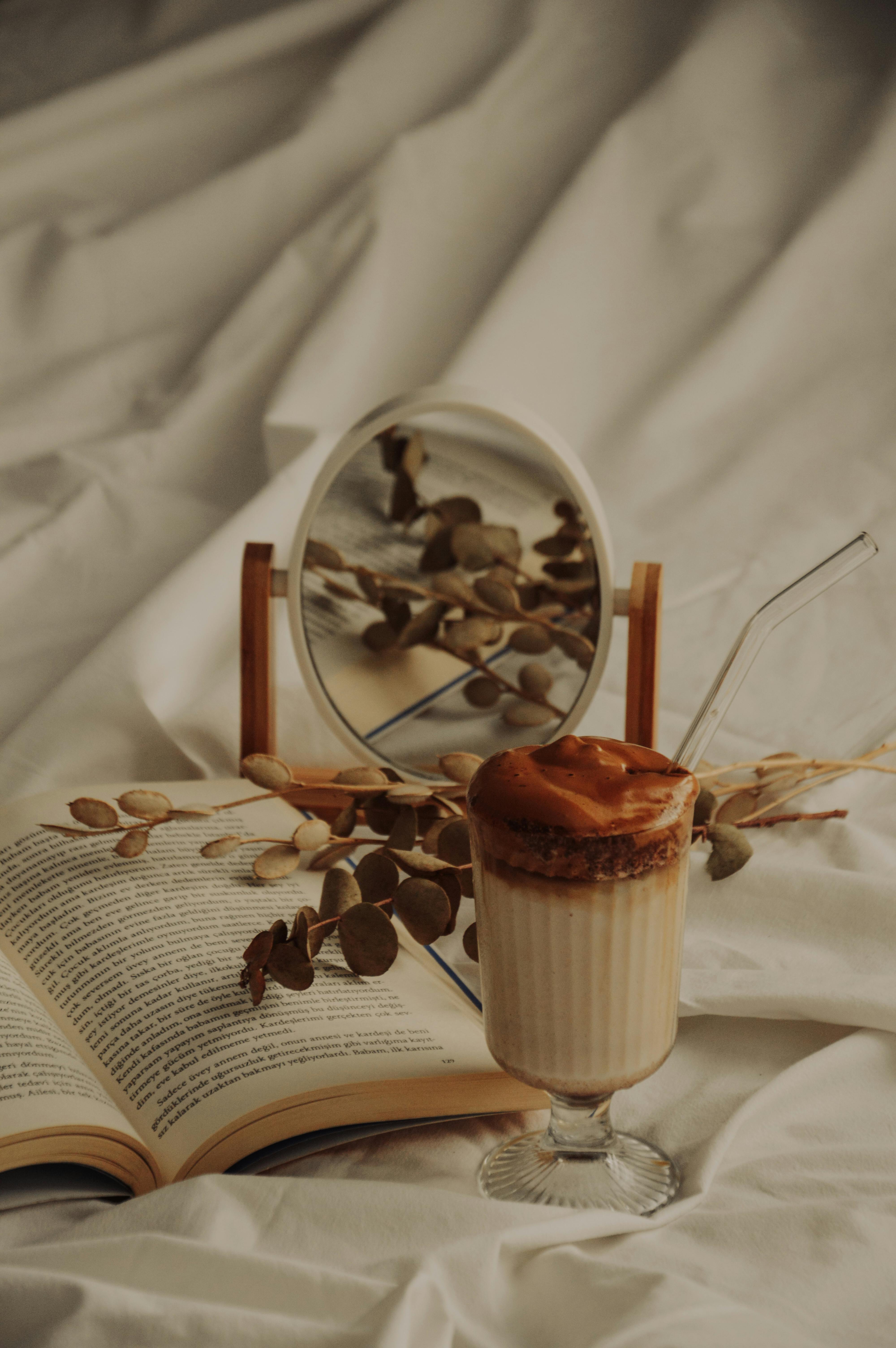 Warm autumn setup with a dalgona coffee, open book, and dried eucalyptus on a soft fabric background.