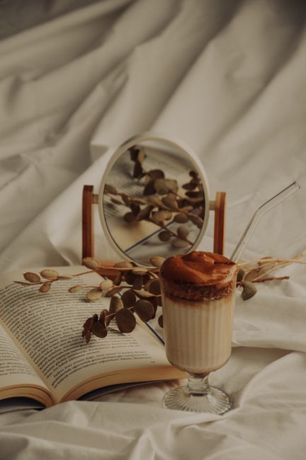 Warm autumn setup with a dalgona coffee, open book, and dried eucalyptus on a soft fabric background.