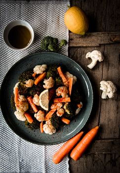 Plate of roasted broccoli, cauliflower, and carrots with lemon and olive oil on rustic table.