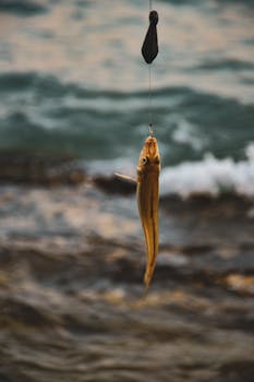 Close-up of a freshly caught fish hanging over ocean waves, captured at sea.