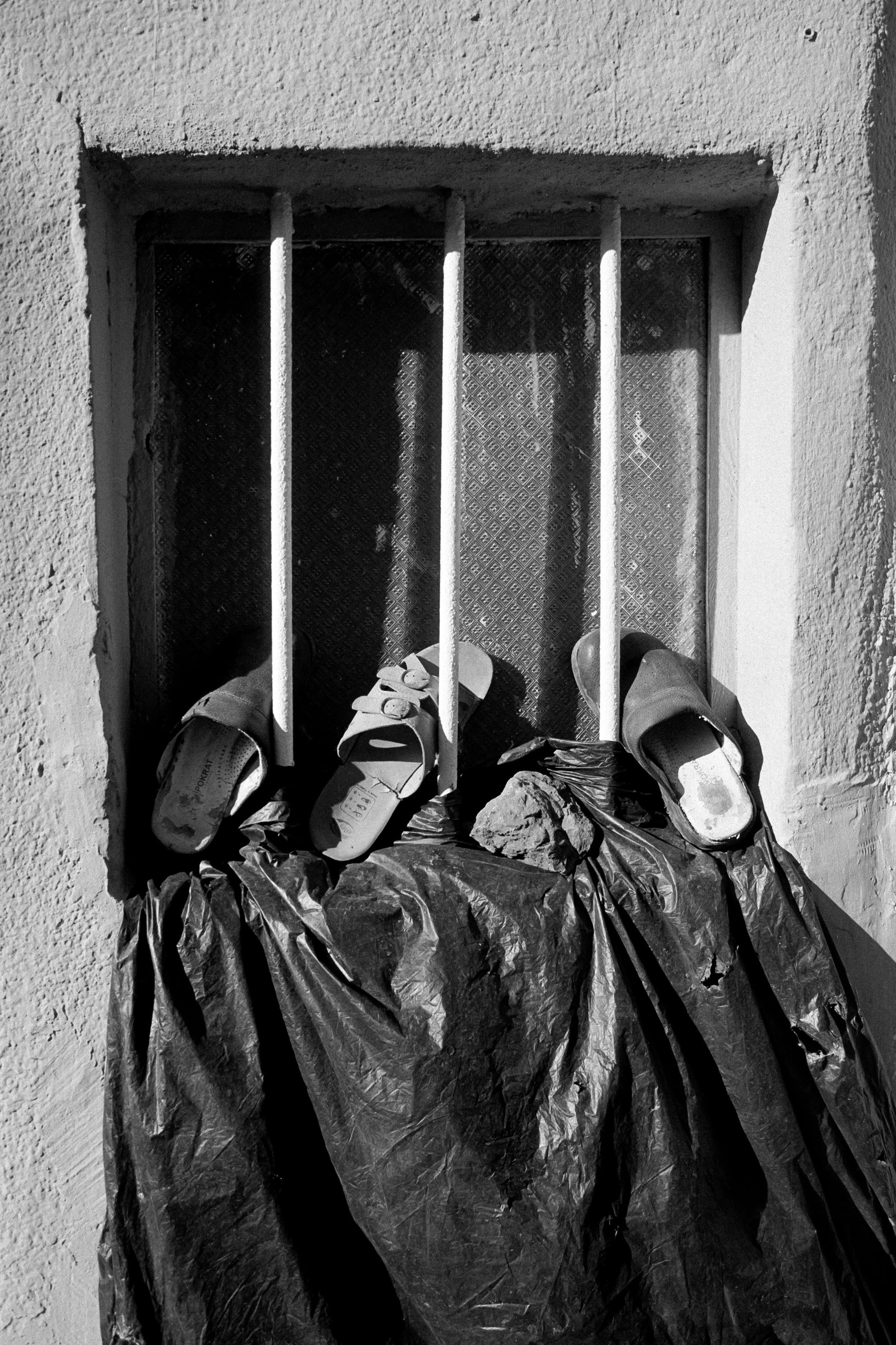 A black and white image features sandals on a barred window in Istanbul, highlighting urban decay.