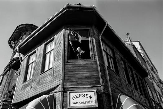 Black and white photo of an elderly woman in İstanbul waving Turkish flag from a historic wooden building.