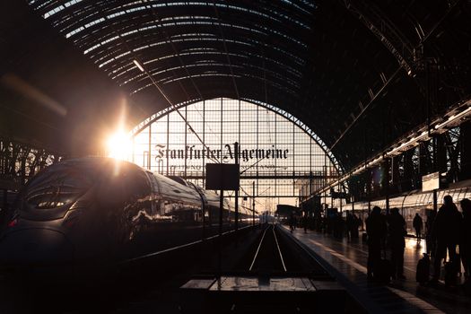 Beautiful sunset at Frankfurt's main train station with travelers and a modern train.