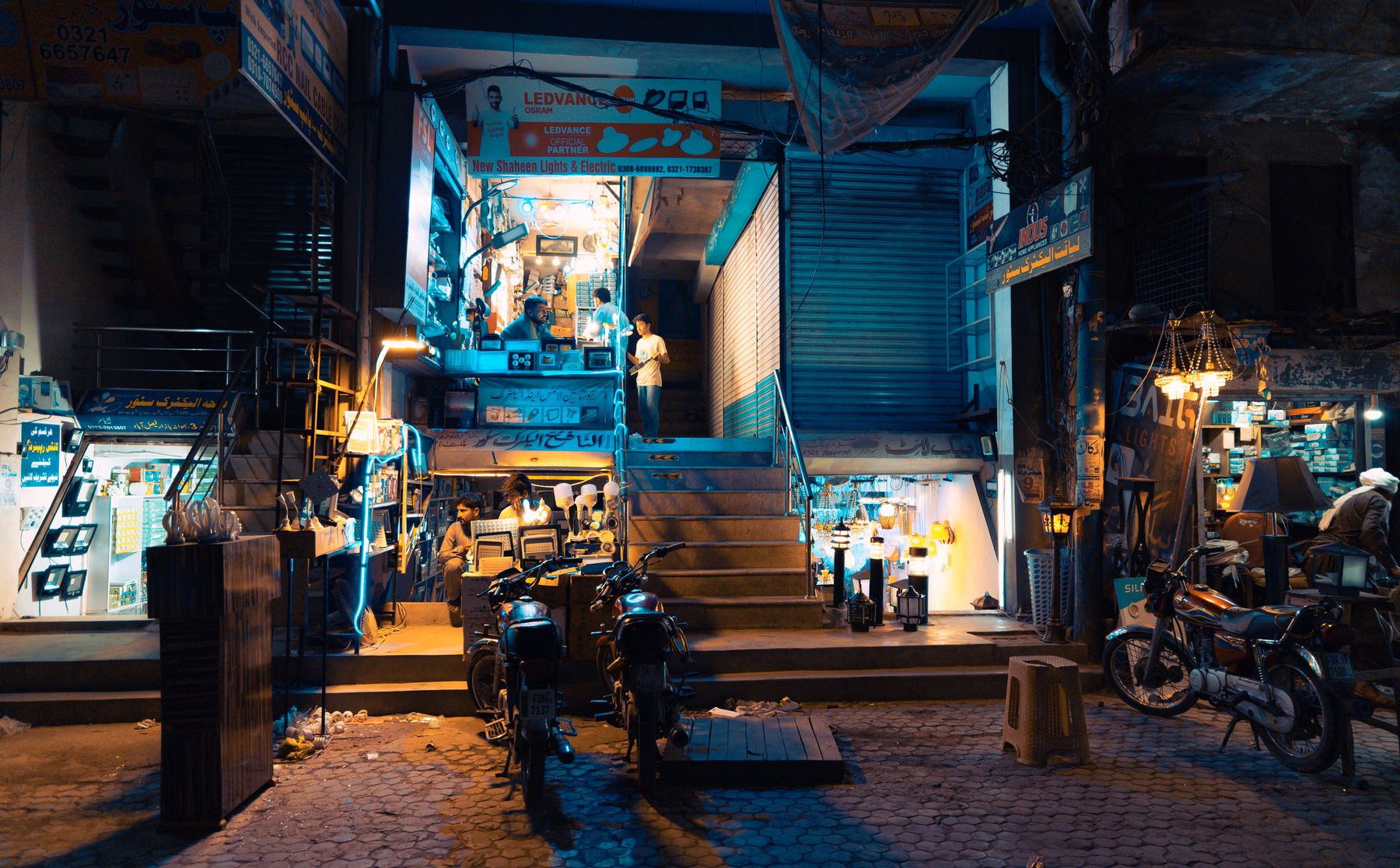 Dynamic nighttime street scene in Faisalabad, Pakistan, showcasing a bustling local market with bright lights.
