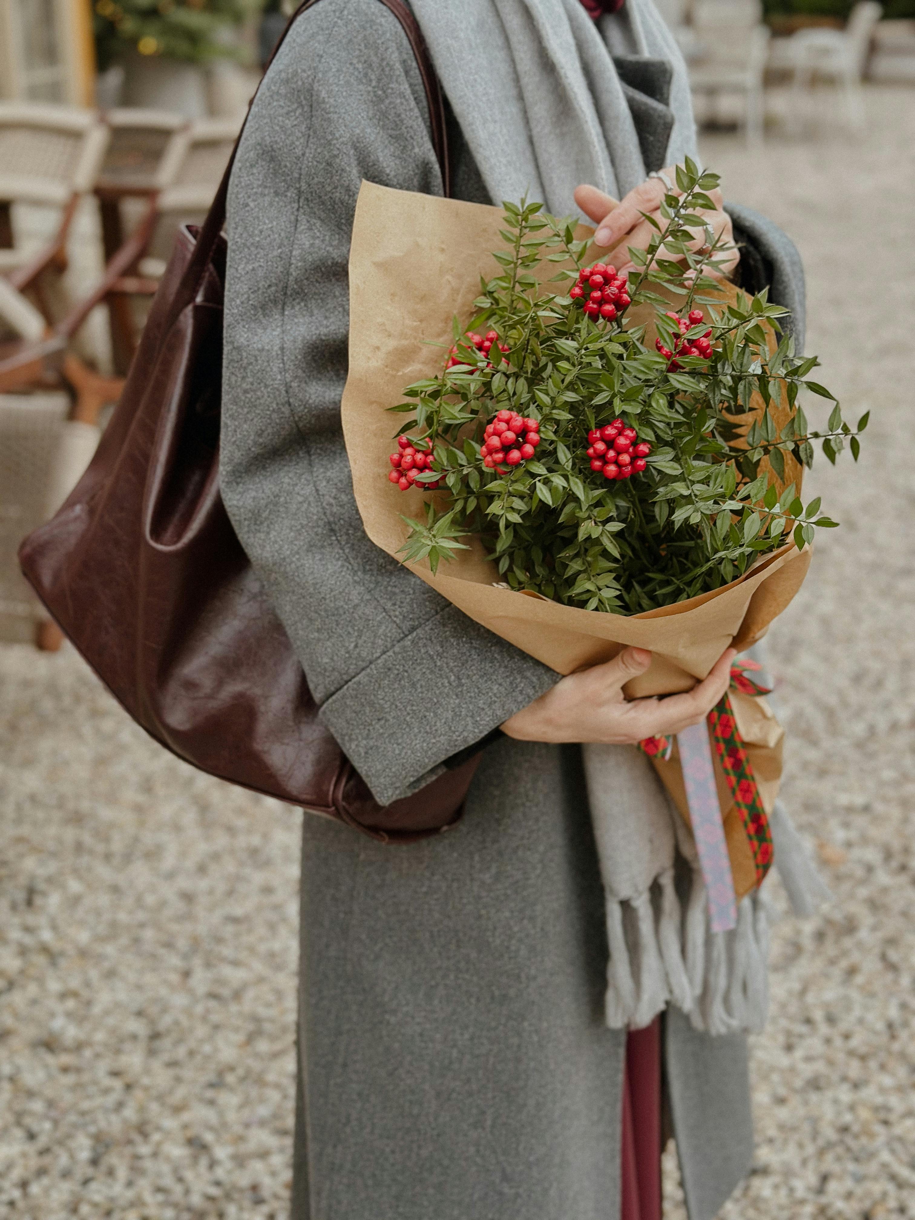 Woman in gray coat holding a bouquet with red berries outdoors. Winter street scene.