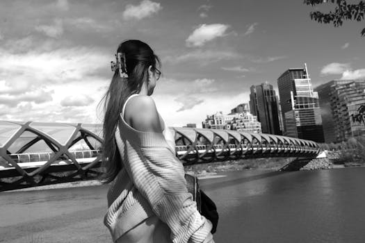 Black and white photo of a woman near Calgary's iconic Peace Bridge, urban skyline in view.