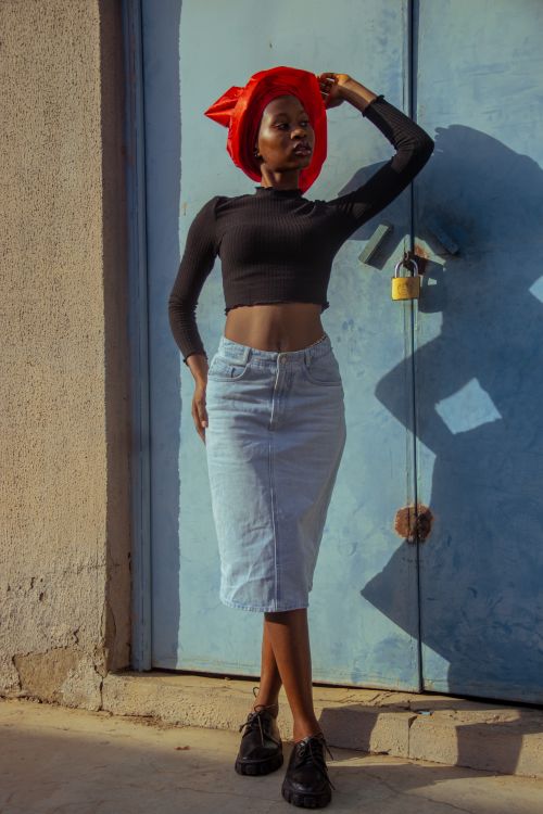 Free Elegant woman in denim skirt and head wrap against blue door, showcasing fashionable style and confidence. Stock Photo