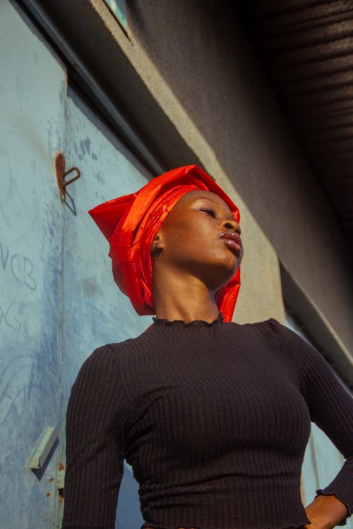 Free A striking portrait of a woman wearing a vibrant orange headscarf under the natural sunlight. Stock Photo