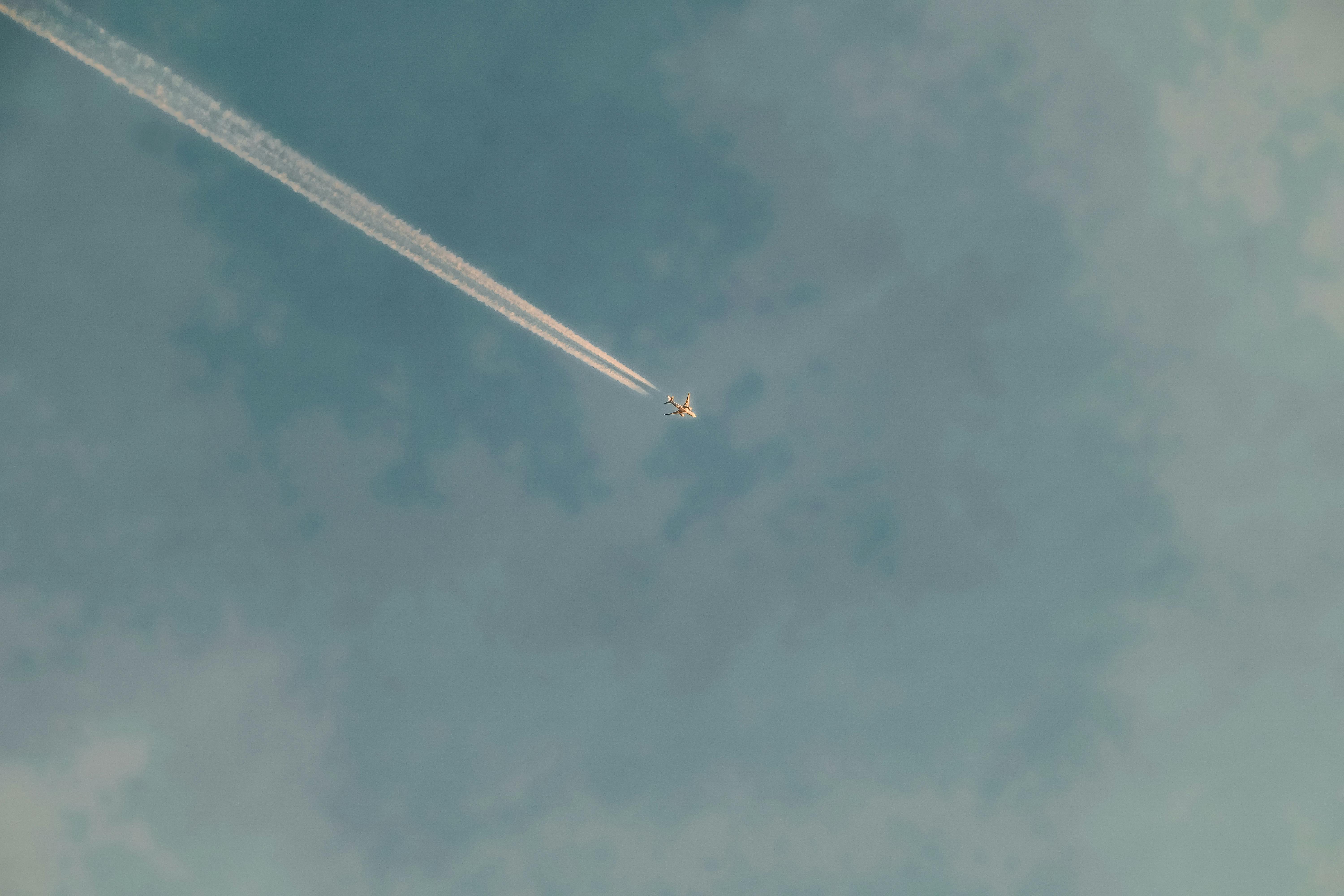 Gratis Gambar minimalis sebuah pesawat terbang dengan jejak kondensasi di langit biru cerah, melambangkan kebebasan. Foto Stok