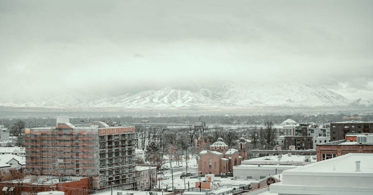 A winter cityscape view in Salt Lake City with snow-covered buildings and mountains in the background.