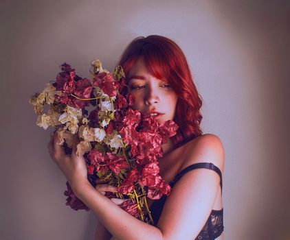Artistic portrait of a redhead woman holding bougainvillea flowers indoors, showcasing beauty and elegance.