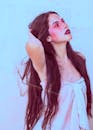 一位留着长发、妆容鲜艳的女人在柔和的背景下抬头仰望