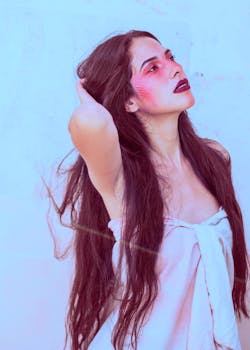 一位妆容鲜艳、长发披肩的女子，在柔和的背景下抬头仰望