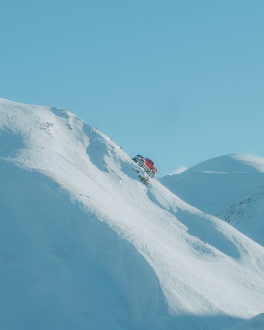 A red SUV climbs a snowy mountain slope in Trabzon, Türkiye, during daytime.