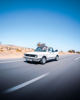 Capture the thrill of a classic convertible speeding on Ankara's scenic highway under clear blue skies.