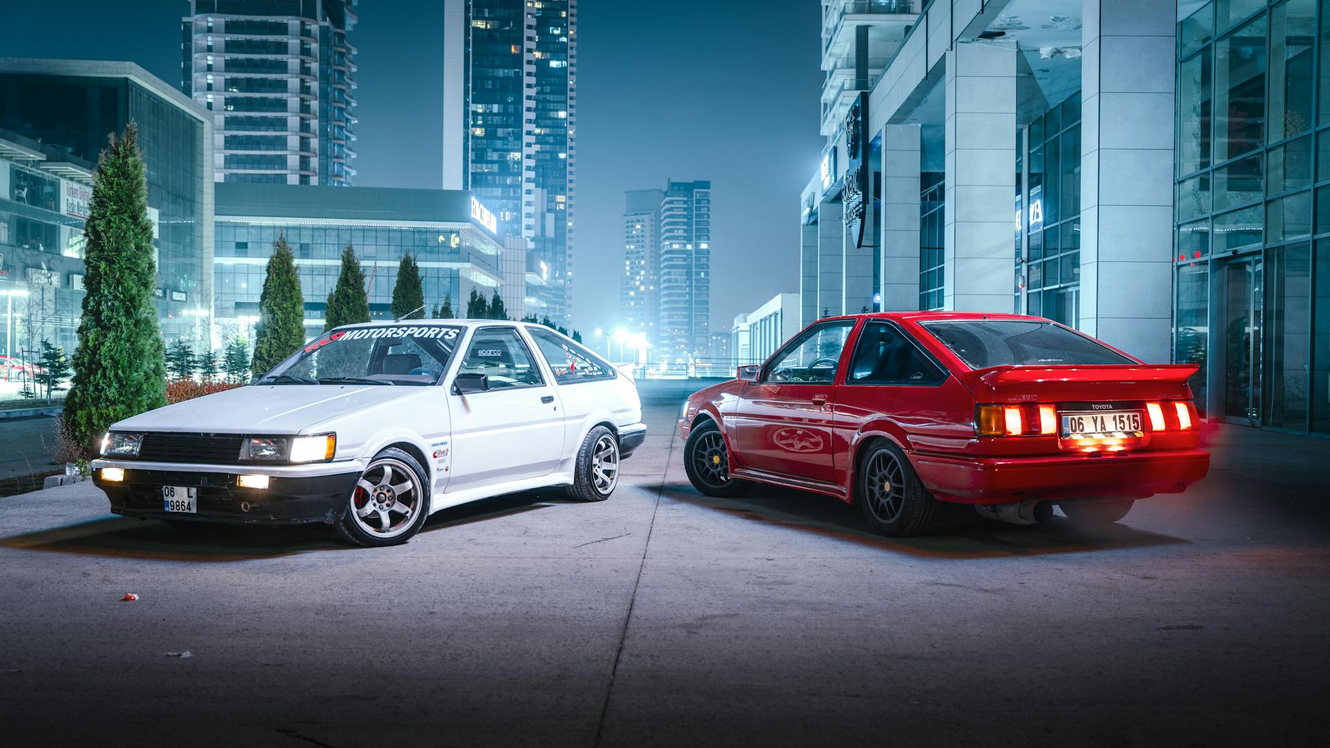 Two classic cars parked in a modern cityscape at night in Ankara, Türkiye.