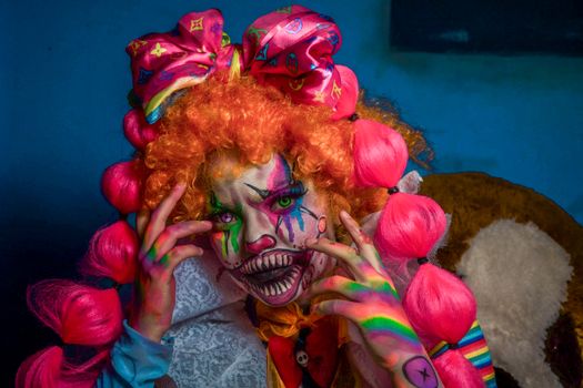Vivid portrait of a clown with colorful makeup and hair in a dramatic indoor setting.