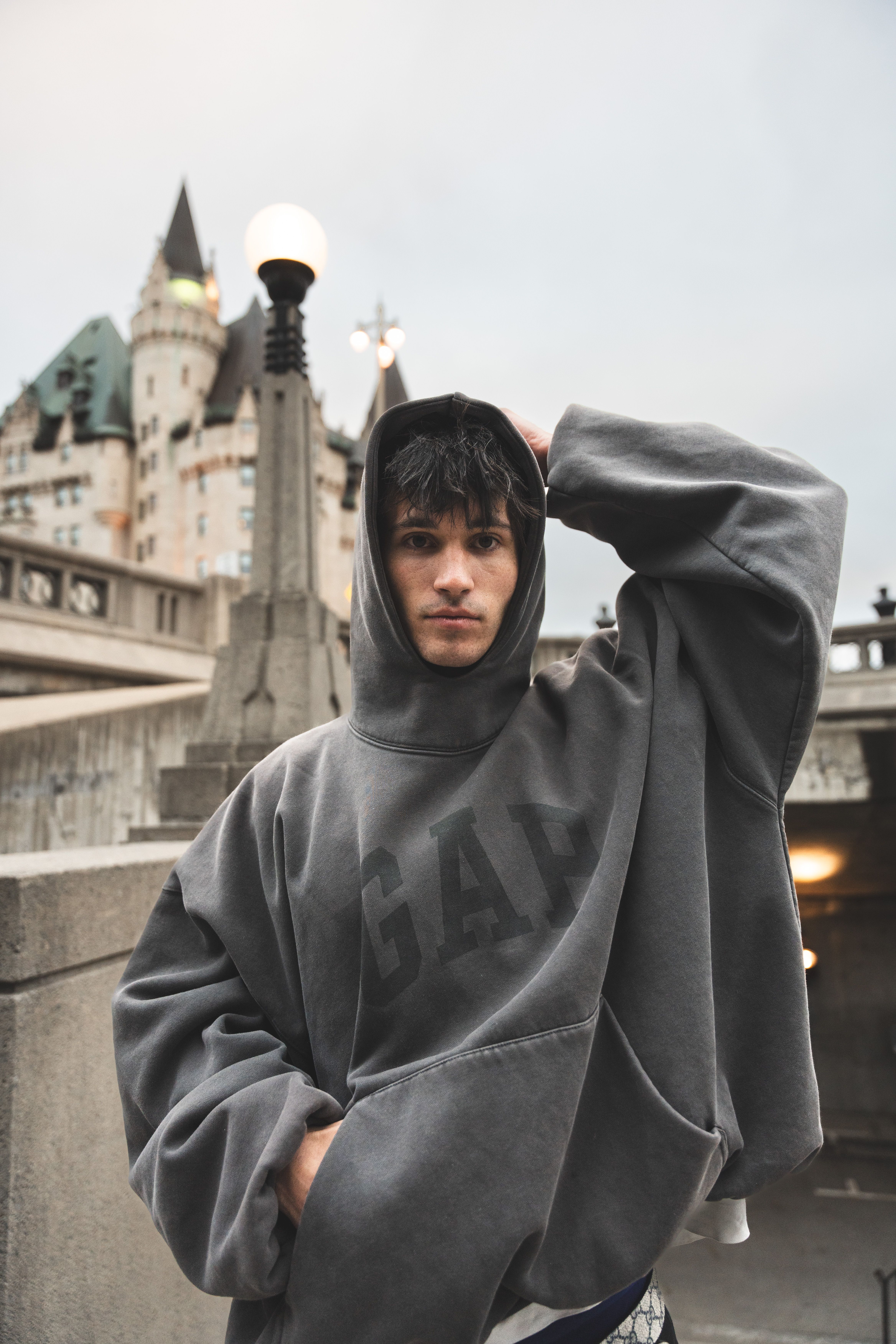 Young man wearing a hoodie poses near a historic building, urban setting.