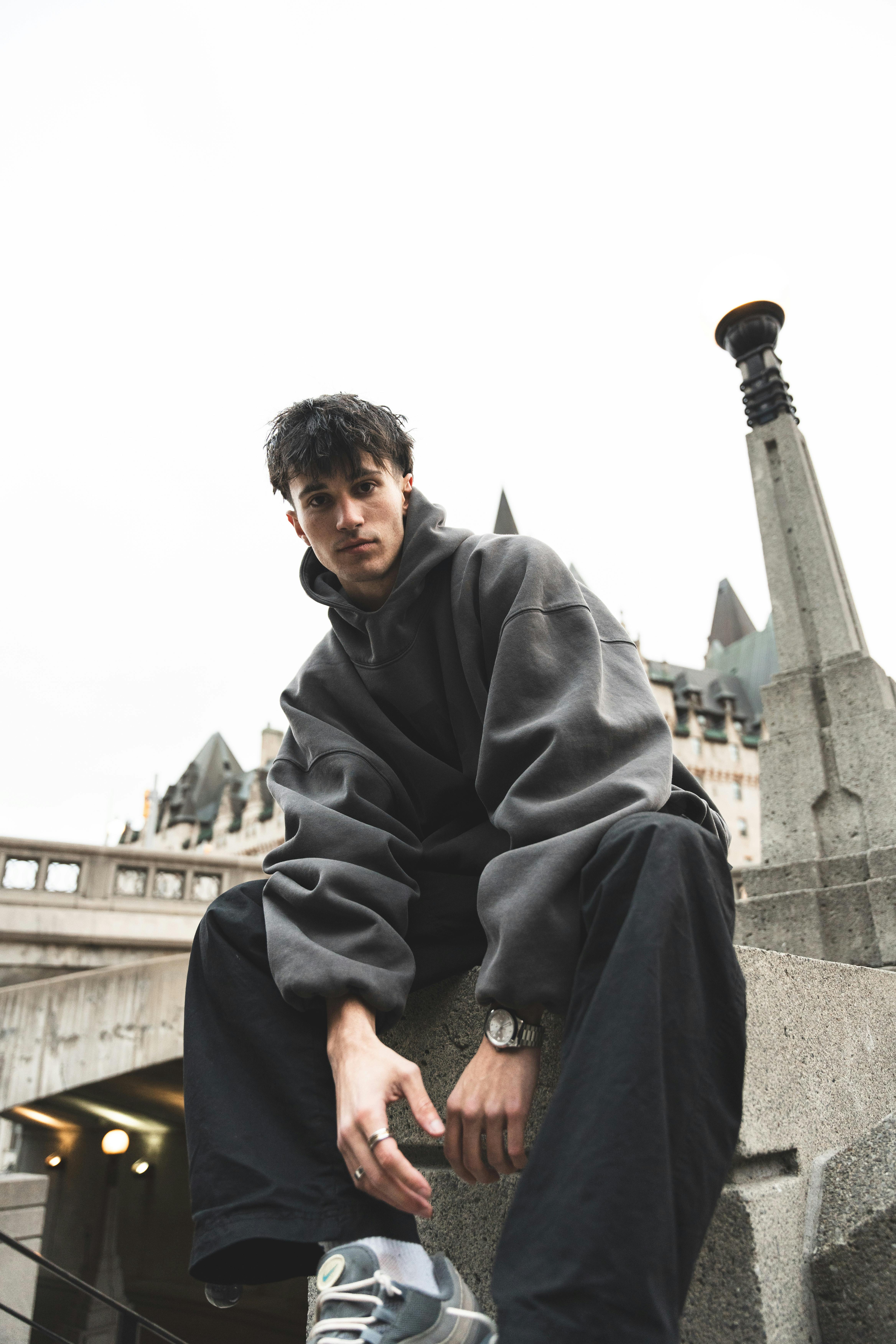 Young man in a cozy hoodie poses against an urban architectural backdrop, exuding a stylish vibe.