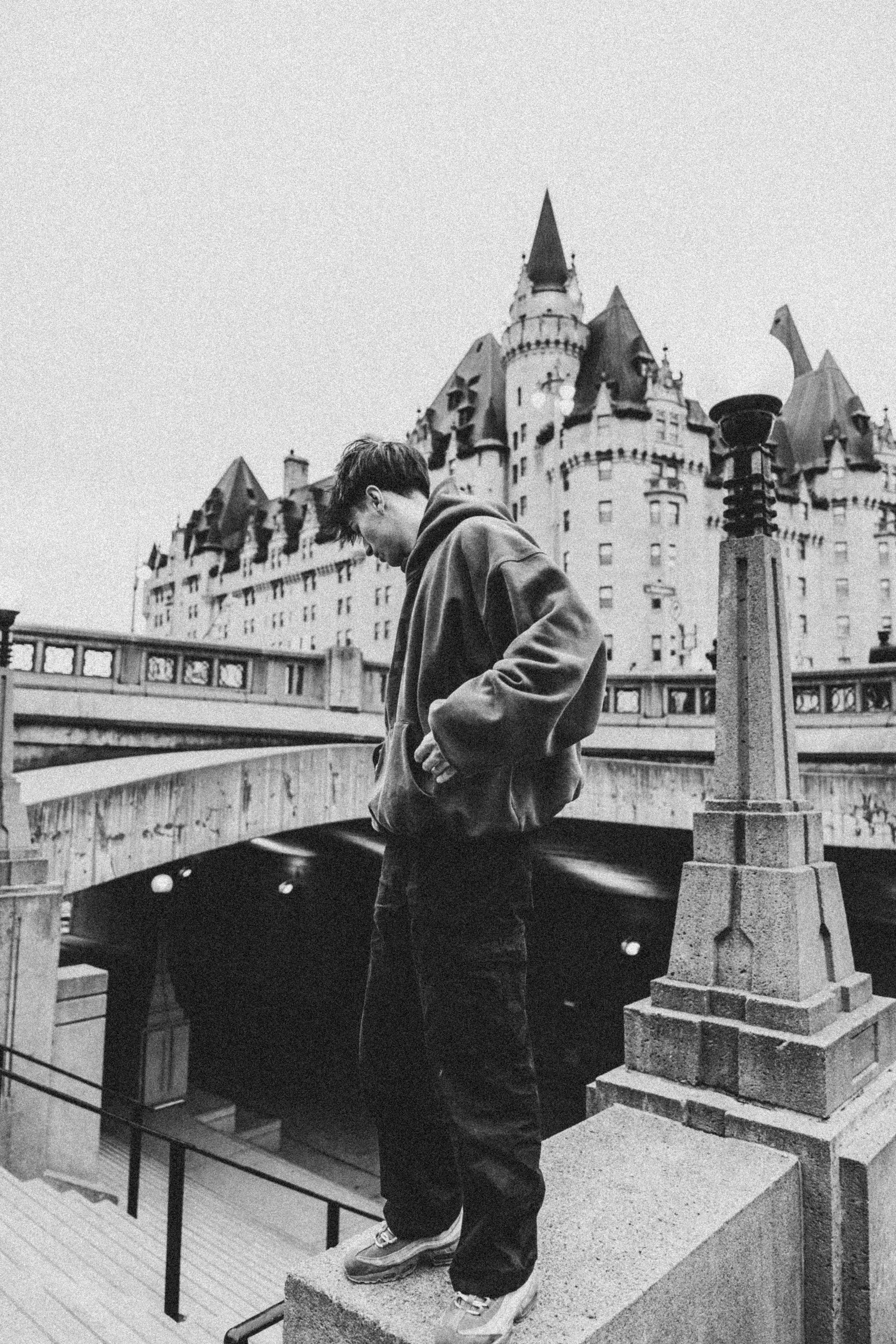 Stylish person in hoodie near gothic architecture in a monochrome photo.
